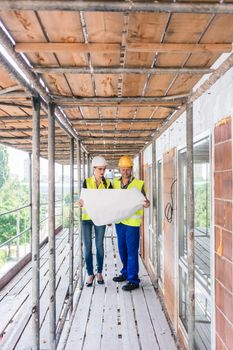 Construction worker and builder on scaffolding reading the plan in front of the building