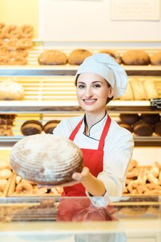 Saleswoman with apron presenting fresh bread in a bakery shop looking into camera