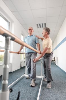 Physiotherapist woman helping senior man in rehabilitation walking on the bars