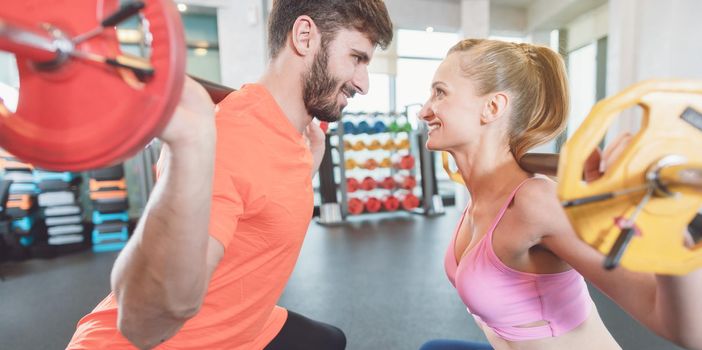 Couple of woman and man in the gym with weights in friendly competition