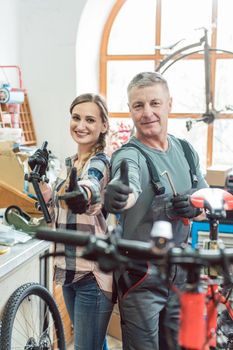 Two bike mechanics in their workshop having a successful day showing their thumbs