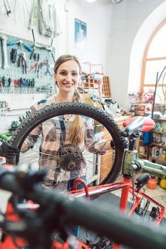 Very happy bike mechanic woman looking through the wheel of bicycle