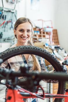 Very happy bike mechanic woman looking through the wheel of bicycle