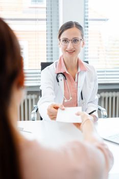 Doctor woman handing slip for prescription drug over to patient