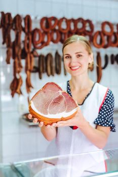 Shop assistant with ham in her butchery showing the meat to customer