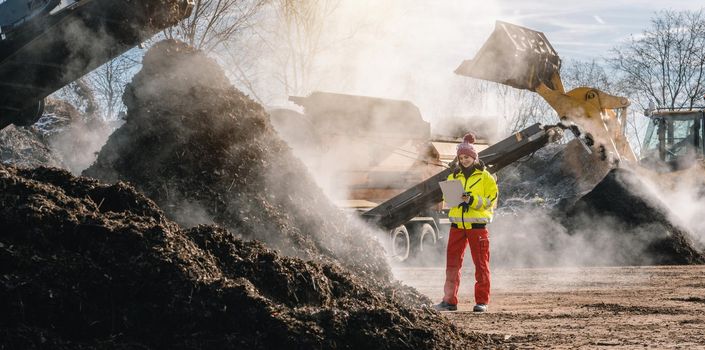 Woman worker standing with clipboard in industrial compost plant