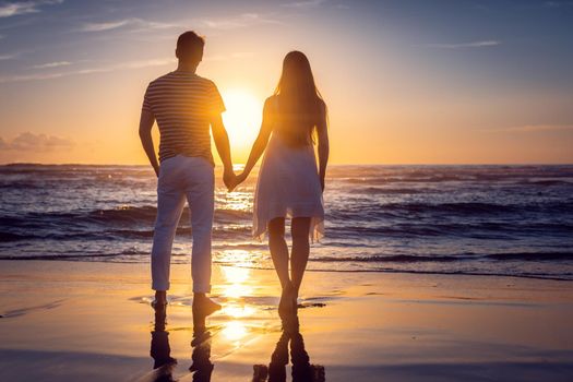 Romantic couple holding hands in their vacation standing on a beach by the sea