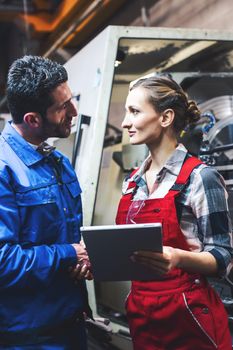 Woman and man manufacturing worker in discussion writing on tablet computer