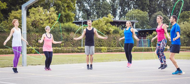 Young and senior male and female in basket ball court exercising and jumping using skipping rope