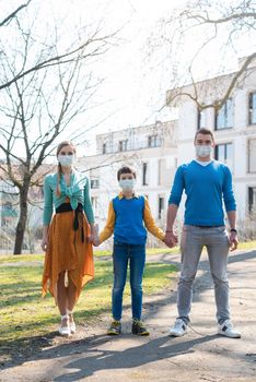 Family having a walk in the sun during corona virus emergency wearing face masks