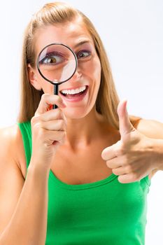 Blonde young woman looking through magnifying glass showing thumb up sign against white background