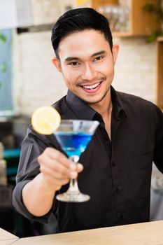 Portrait of handsome man holding blue cocktail at bar