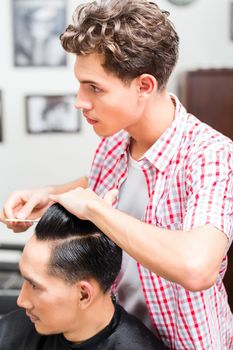 Professional young male hairdresser hairstyling the client's hair