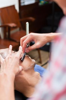 Close-up of professional barber shaving with razor in salon