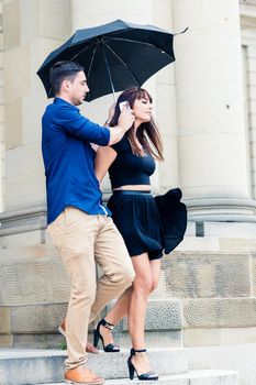 Young man holding umbrella and cellphone near his girlfriend's ear