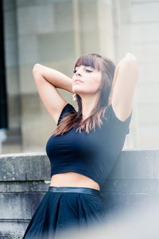 Close-up of beautiful young woman leaning on wall putting hands behind the head