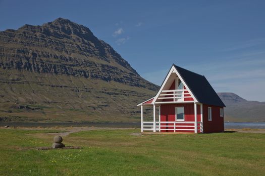 Traditional red painted wooden panel house with mighty Holmatindur mountain in the background in Eskifjordur, East Iceland.
