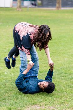 Man balancing his girlfriend on his legs, lying on green grass
