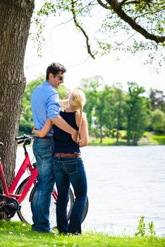 Rear view of young couple standing near the lake with bicycle