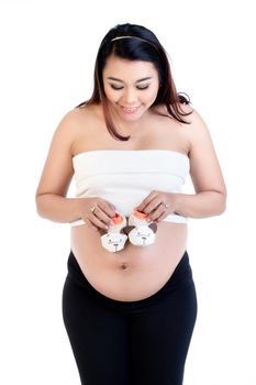 Smiling pregnant woman holding pair of baby shoes over her belly isolated over white background