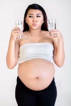 Close-up of confused pregnant woman holding milk and water glass isolated over white background