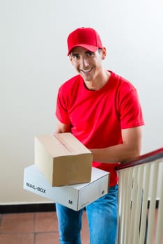 Smiling delivery man holding two cardboard boxes leaning on railing