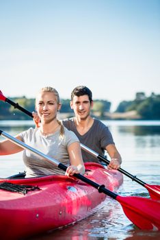 Smiling young couple using paddles while kayaking on lake