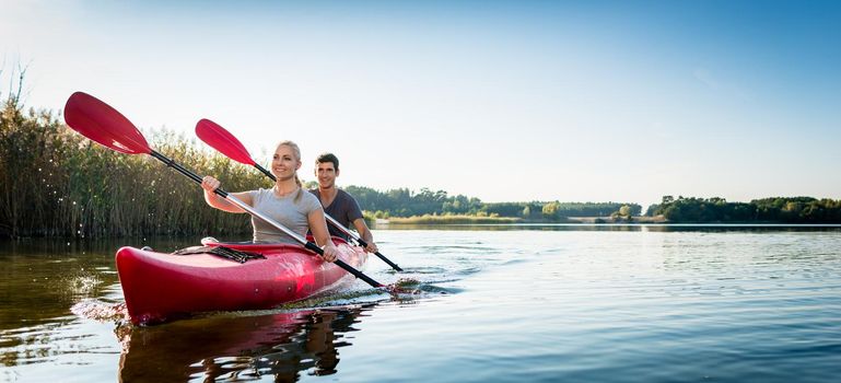 Close-up of beautiful young couple sailing kayak on idyllic lake
