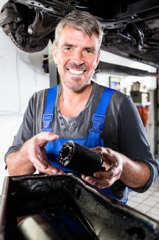 Portrait of smiling mature man holding the oil filter in the auto repair shop