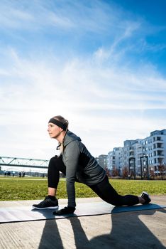 Low-angle view of a determined young woman stretching her leg while kneeling on a mat outdoors in summer