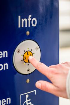 Woman pressing info button of assistance machine in train station, only finger to be seen