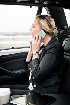 Side view of young businesswoman using smartphone while travelling in the car