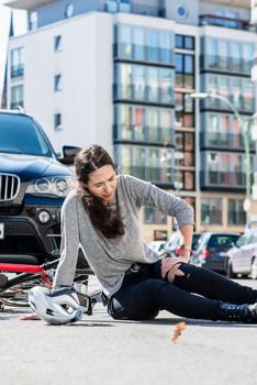 Full length of an injured young woman experiencing severe pain caused by knee sprain or fracture after bicycle accident in the city