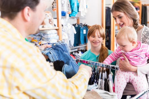 Close-up of smiling family looking at clothes on rail in shopping mall