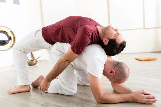 Two flexible healthy men performing acroyoga in class