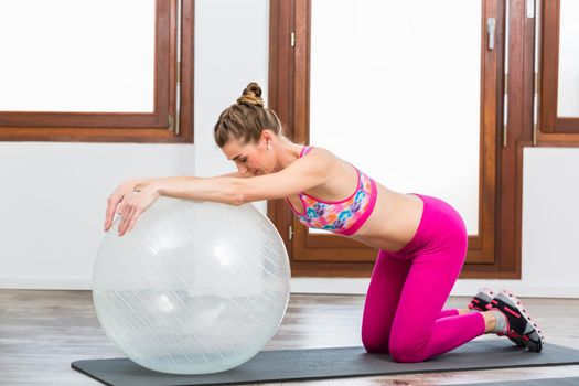 Side view of woman doing exercise on pilates ball on exercise mat in gym