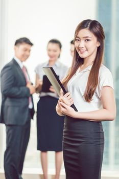 Smiling young businesswoman standing in front of colleague discussing on digital tablet