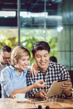Smiling young couple looking at digital tablet with coffee cup and cellphone on table in the cafe