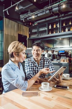 Smiling young Woman looking at the digital tablet in her boyfriend's hands in the cafe