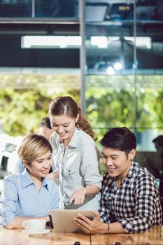 Group of happy friends looking at digital tablet in the coffee shop