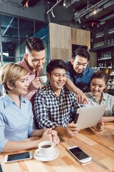 Portrait of smiling young friends looking at digital tablet in the coffee shop