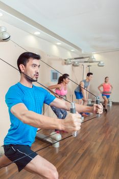 Portrait of a determined fit young man exercising with the resistance bands of an anchor gym system mounted on wall in a trendy fitness club