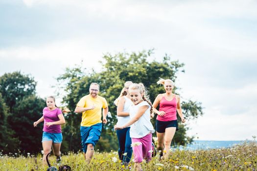 Family running on a meadow with flowers for sport