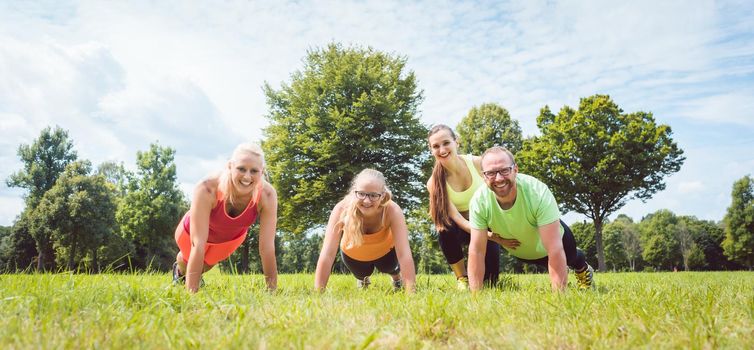 Family doing push-ups in nature under guidance by a fitness coach on grass