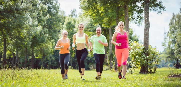 Family with personal Fitness Trainer jogging on a meadow