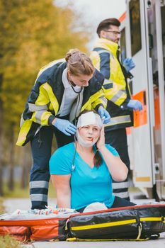 Emergency medics dressing head wound of injured woman after accident
