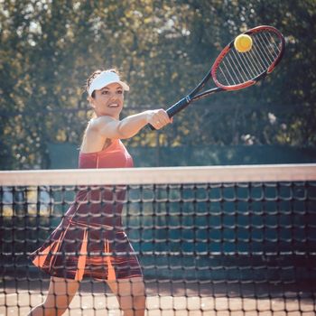 Woman in red sport dress playing tennis hitting the ball