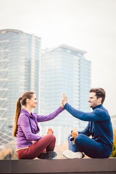 Woman and man giving hi-five after fitness sport in a city, in the background a high-rise building is to be seen