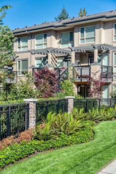 Fresh lawn in front residential townhouse building on blue sky background.