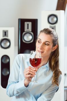 Woman having glass of wine in front of Hi-Fi speakers enjoying the drink and the music